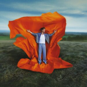 Albumo viršelis vaizduoja vyrą, stovintį atviroje pievoje, apsuptą dramatiškai išsiskleidžiančios ryškiai oranžinės medžiagos. Ji atrodo tarsi audringas, vėjo pakeltas audinys ar didžiulis spalvinis pliūpsnis, kontrastuojantis su ramiu, žalsvai mėlynu peizažu fone. Vyras vilki šviesiai mėlyną, blizgų kostiumą ir baltus marškinėlius, o išskėstos rankos suteikia kompozicijai laisvės, ekspresijos ir pasidavimo gamtai pojūtį. Bendras įspūdis labai dinamiškas, modernus ir vizualiai ryškus, tarsi perteikiantis energijų susiliejimą tarp žmogaus ir aplinkos.