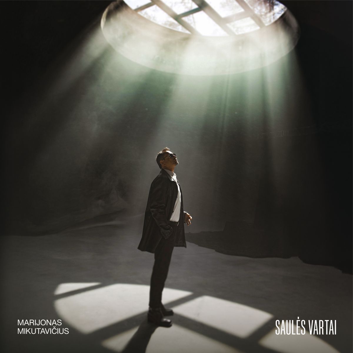 Marijonas Mikutavičius Saulės Vartai vinilinė plokštelė Albumo viršelis perteikia dramatišką, kinematografišką nuotaiką. Jame matomas vienišas vyras, stovintis po dideliu apvaliu šviesos spinduliu, krintančiu iš viršuje esančio apskrito lango. Šviesa sklinda tarsi pro saulės vartus – stipri ir kryptinga, apšviečianti figūrą iš viršaus ir sukurianti ryškių šešėlių ant grindų. Vyras apsirengęs tamsiu paltu ir šviesiais marškiniais, žiūrintis aukštyn, tarsi į šviesos šaltinį. Aplinka tamsi, beveik tuščia, todėl šviesos srautas ir žmogus tampa pagrindiniais akcentais.